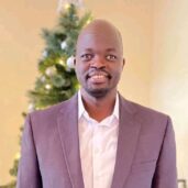 A man in a suit and tie standing next to a christmas tree.