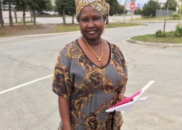 A woman standing on the side of a road holding papers.